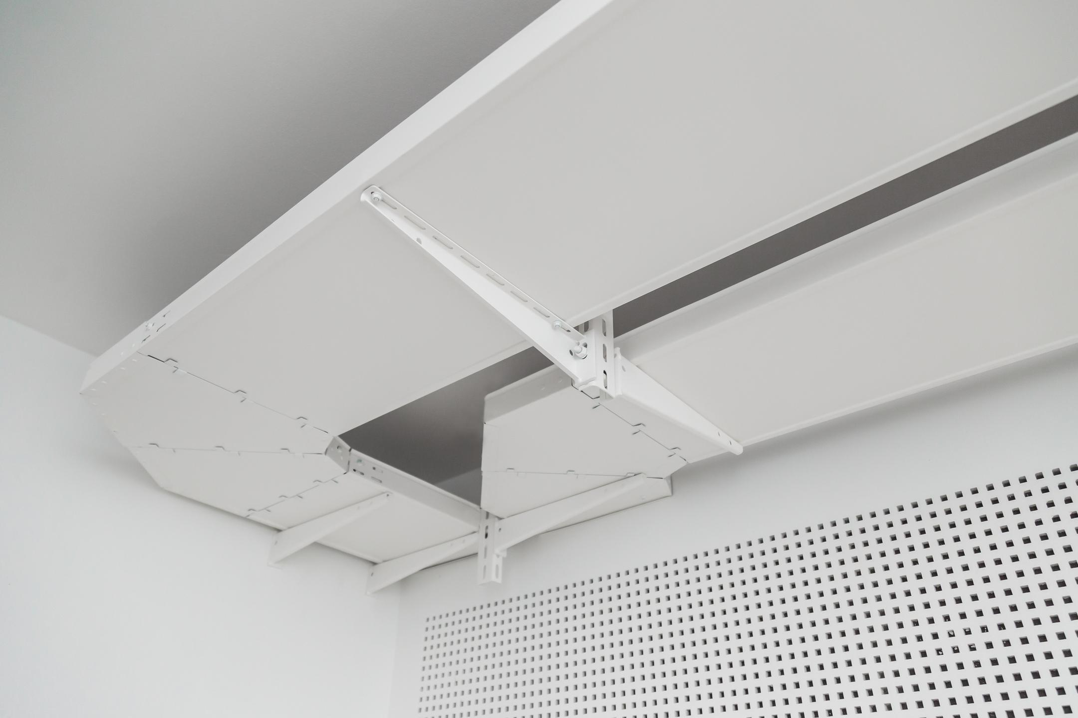Weiße Decke mit abgehängter ungelochter Kabelrinne in Weiß mit perforierter Wandverkleidung