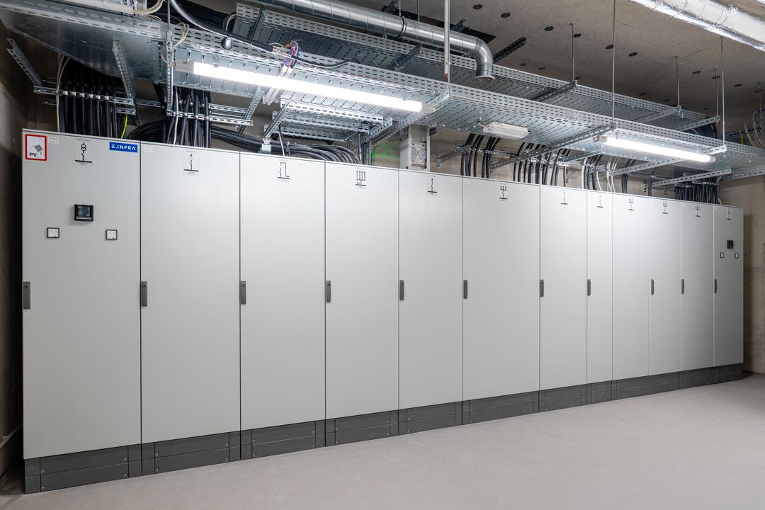 Reihe moderner Schaltschrankanlagen in einem Technikraum mit Kabeltrassen oben