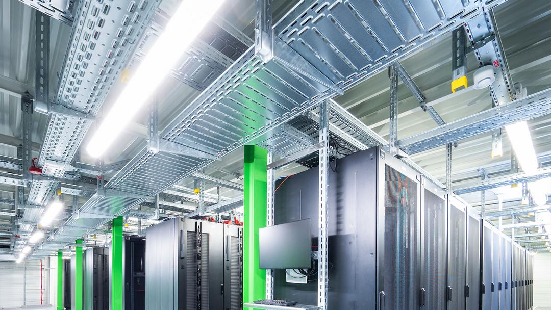 Rechenzentrum mit Serverracks, grünen Stützen und verzinkten Kabeltrassen zur strukturierten Kabelführung unter der Decke.
