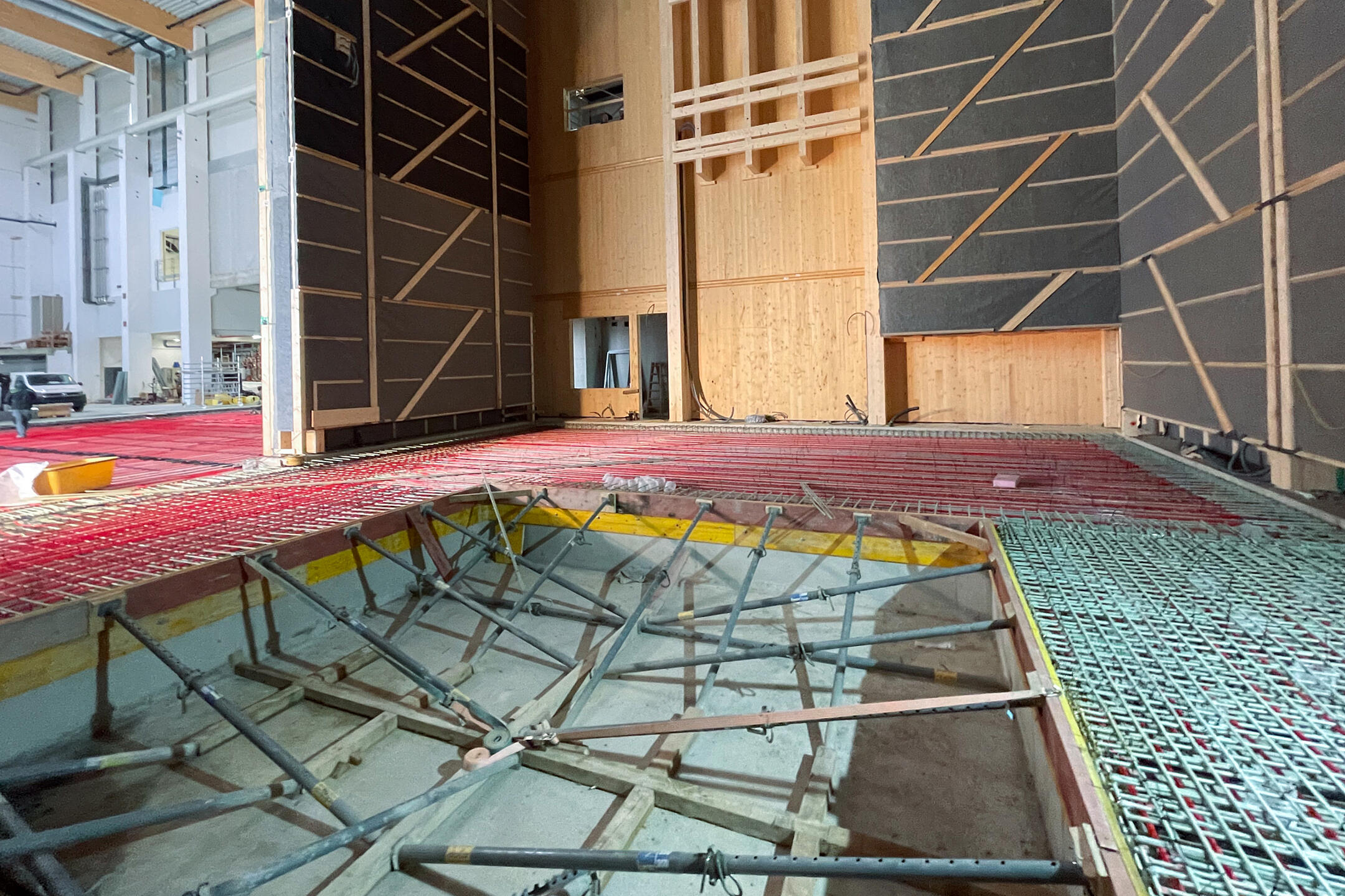 Innenansicht eines im Bau befindlichen Industriegebäudes mit Holzbauwänden, GFK-Bewehrung und Schalung für eine Betonplatte sowie sichtbaren Installationen im Rohbauzustand.