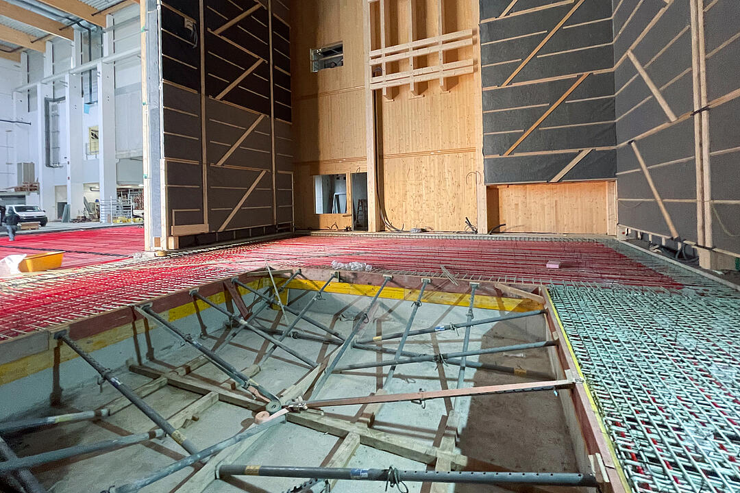 Innenansicht eines im Bau befindlichen Industriegebäudes mit Holzbauwänden, GFK-Bewehrung und Schalung für eine Betonplatte sowie sichtbaren Installationen im Rohbauzustand.