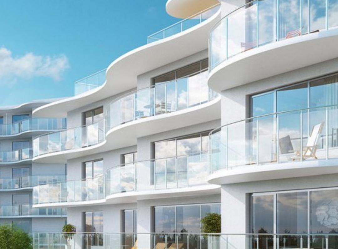 Modernes Wohngebäude mit Glasbalkonen, bodentiefen Fenstern und geschwungener weißer Fassade, blauer leicht bewölkter Himmel