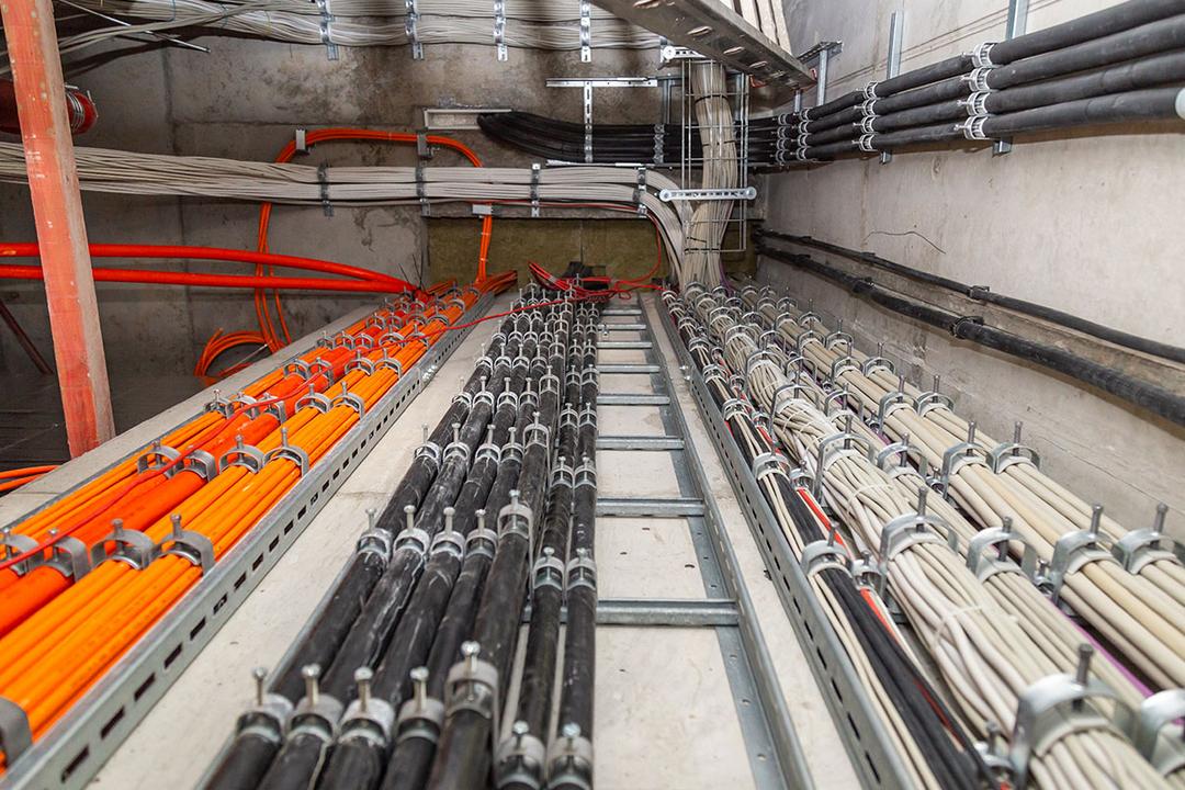 Bündel von orangefarbenen, schwarzen und weißen Kabeln befestigt an Kabelleitern an einer Gebäudeinnenwand