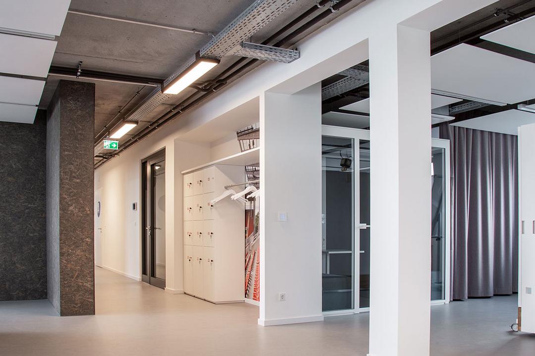 Blick in einen offenen, von Säulen gestützten Arbeitsbereich, durch den eine von der Decke hängende Kabelrinne für Deckenlampen verläuft.