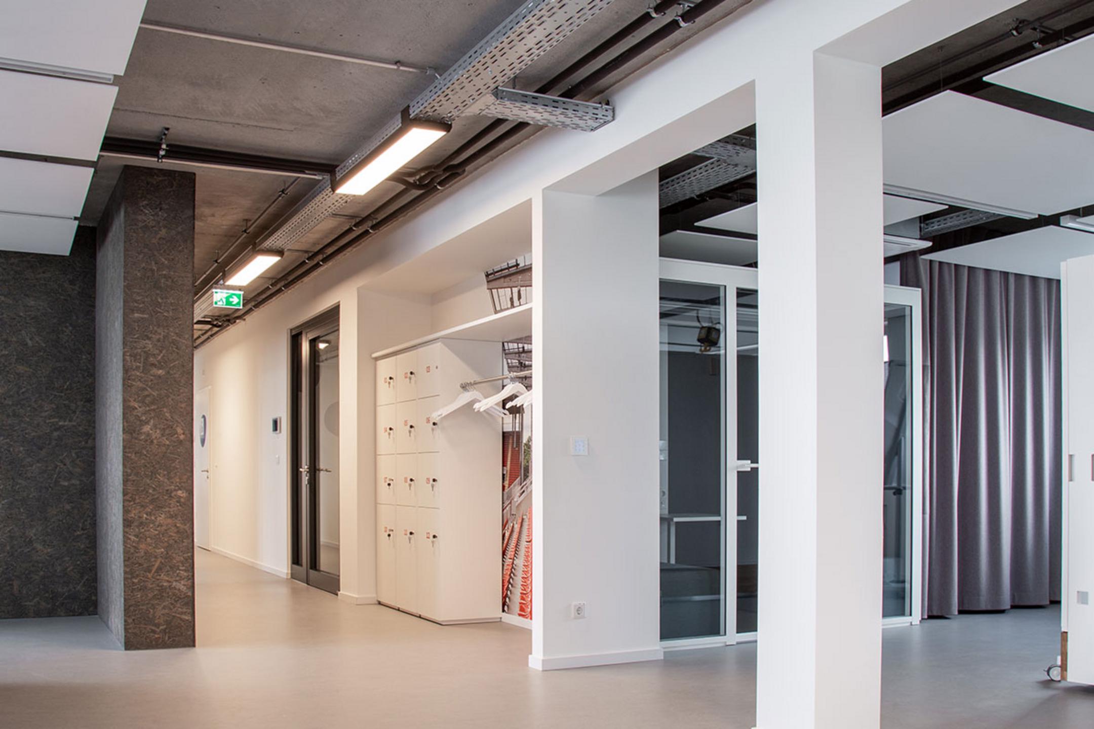 Blick in einen offenen, von Säulen gestützten Arbeitsbereich, durch den eine von der Decke hängende Kabelrinne für Deckenlampen verläuft.