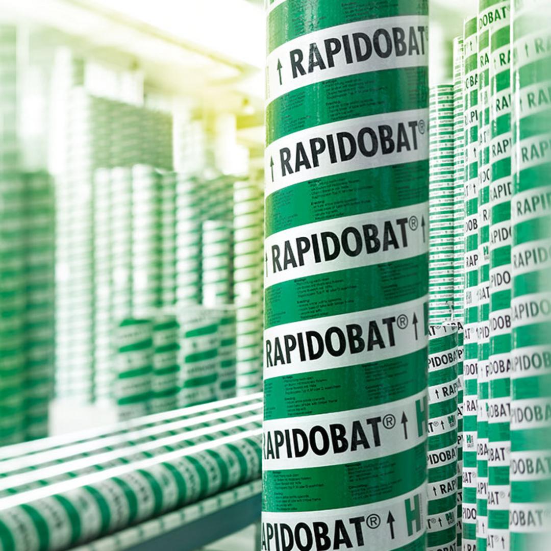 Grüner Schalkörper mit Aufschrift 'Rapidobat' im Vordergrund, im unscharfen Hintergrund stehen und liegen weitere Schalungskörper