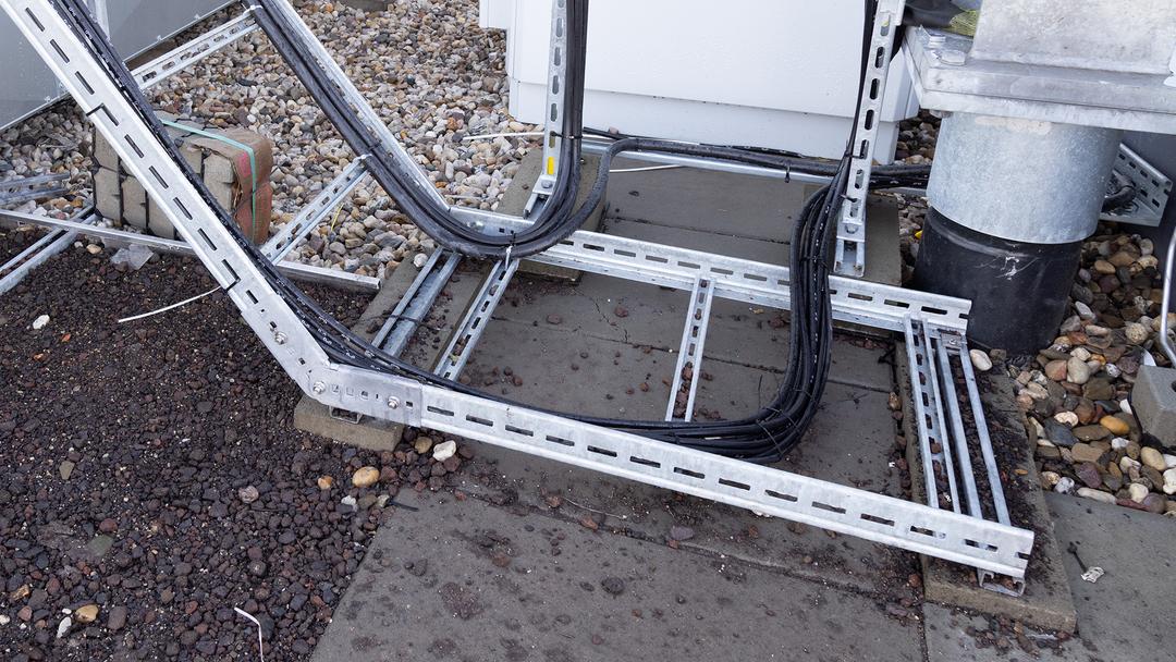 Kabeltrassen-System auf einem Flachdach mit verzinkten Montageschienen, Betonauflagen und geführten Stromkabeln.