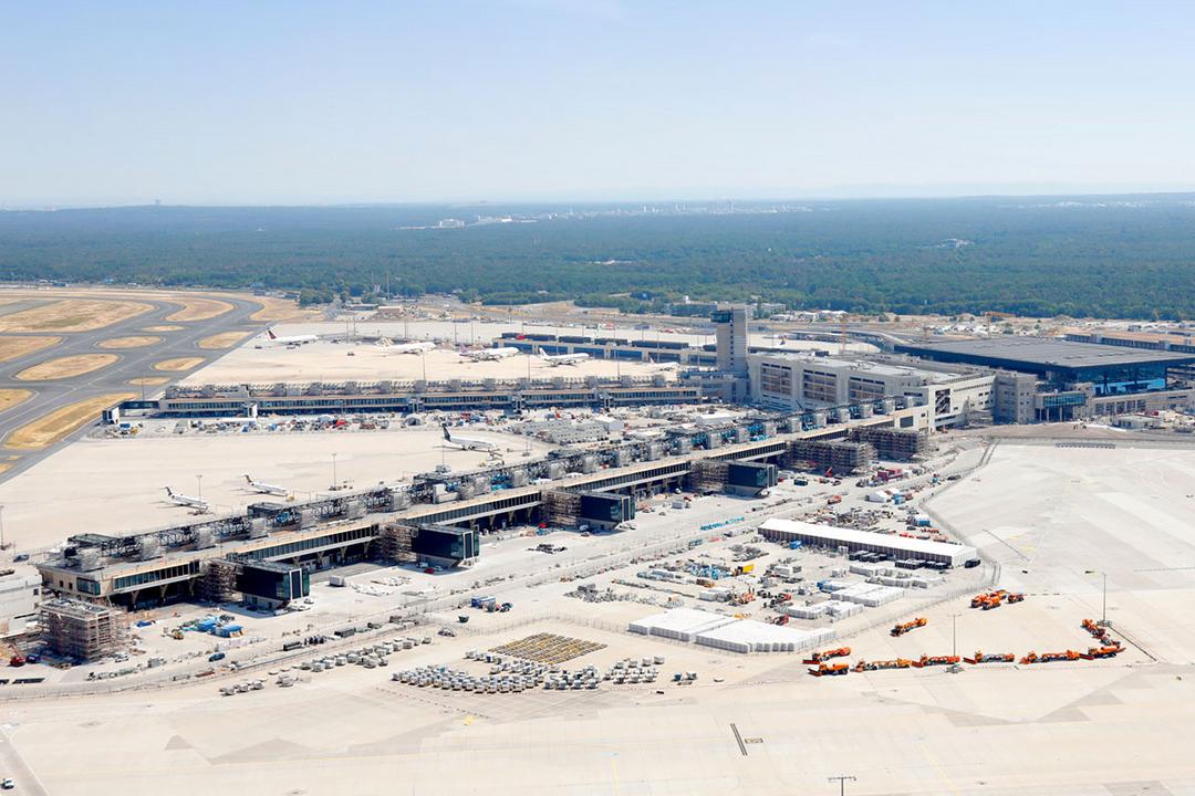 Luftaufnahme des Flughafen-Terminalbaus mit Rollfeldern, Flugzeugen, Gebäuden und umliegendem Waldgebiet