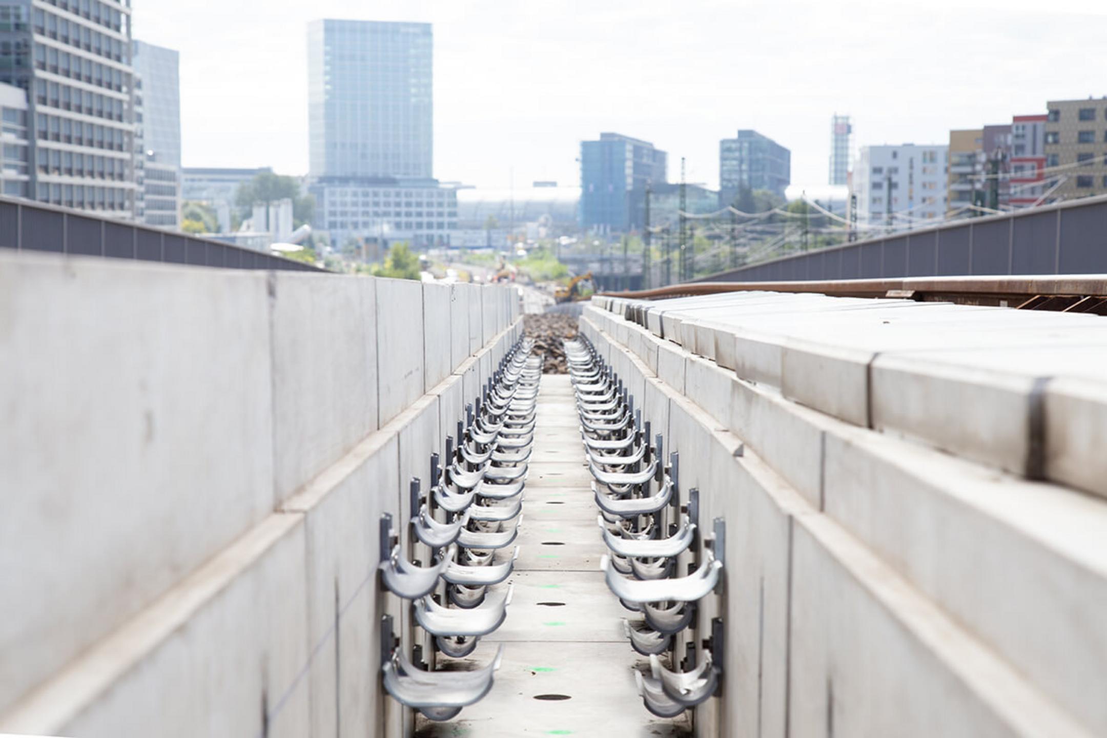 Detailaufnahme der Kabeltragwannen an Bahnschienen mit Berliner Hochhäusern im Hintergrund.