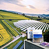 Trade fair counter with brochures on it in front of a large photo wall showing a ground-mounted photovoltaic system.