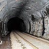 Dunkler Eisenbahntunnel mit markanten Kalkablagerungen an den Wänden, Schienen