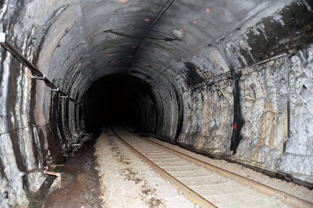 Dunkler Eisenbahntunnel mit markanten Kalkablagerungen an den Wänden, Schienen