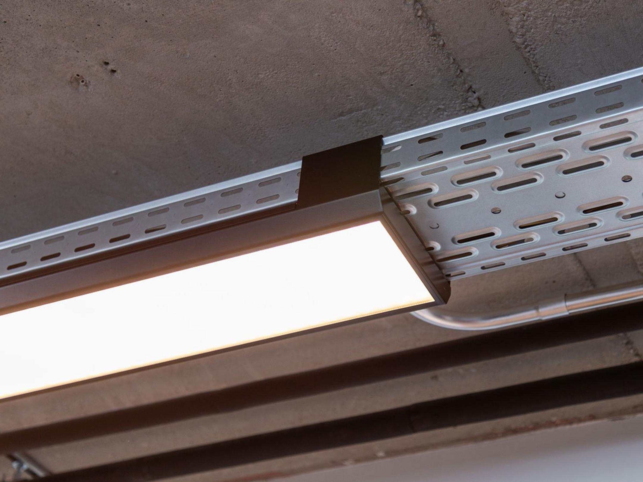 Eine von der Decke hängende, nicht lackierte Kabelrinne für Deckenlampen.