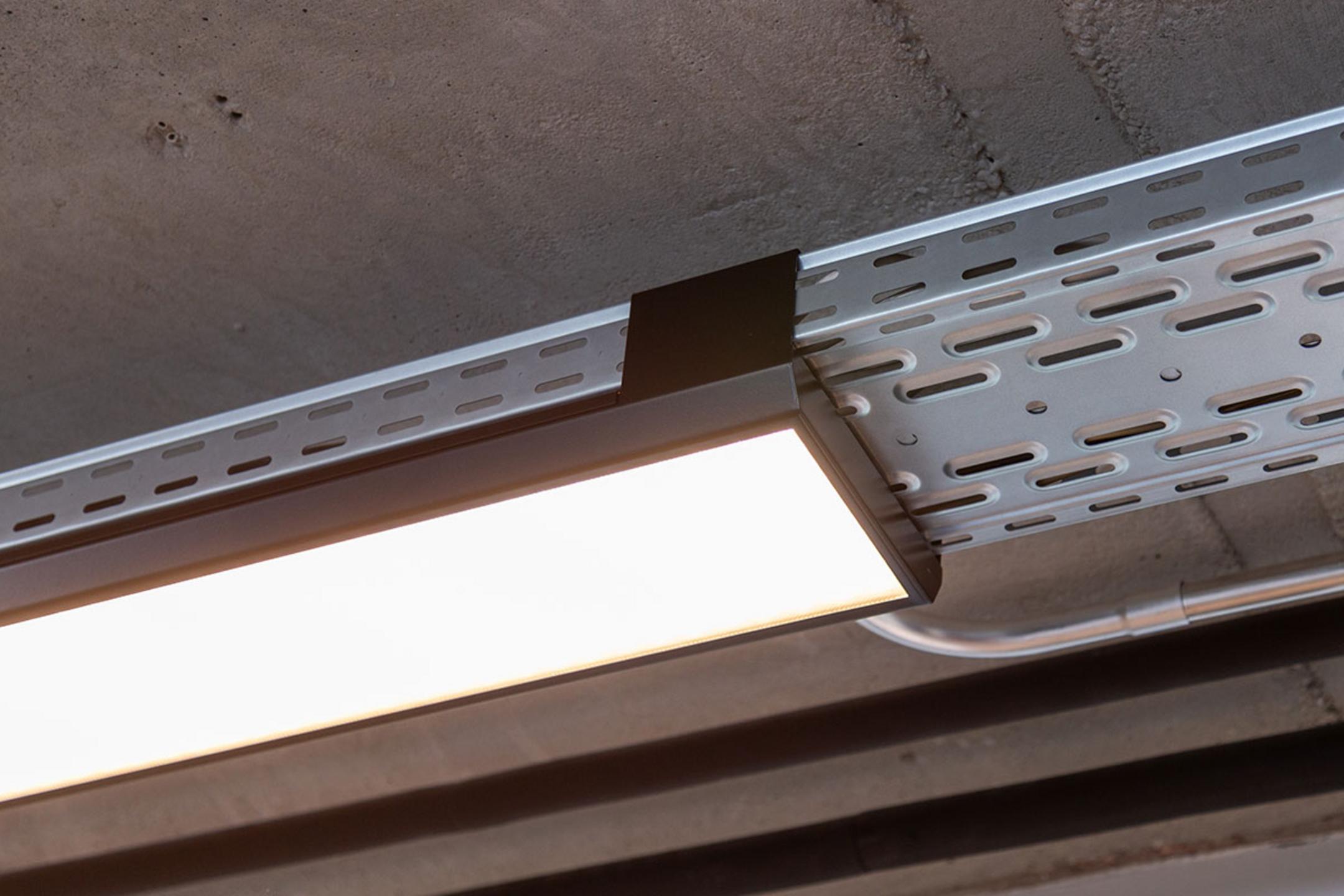 Eine von der Decke hängende, nicht lackierte Kabelrinne für Deckenlampen.