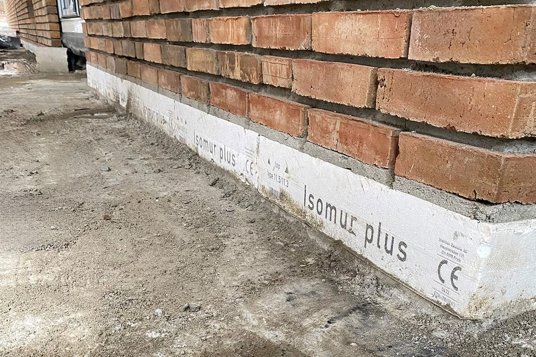 Nahaufnahme eines Sockels mit Isomur Plus Dämmstoff unter einer Ziegelmauer auf einer Baustelle
