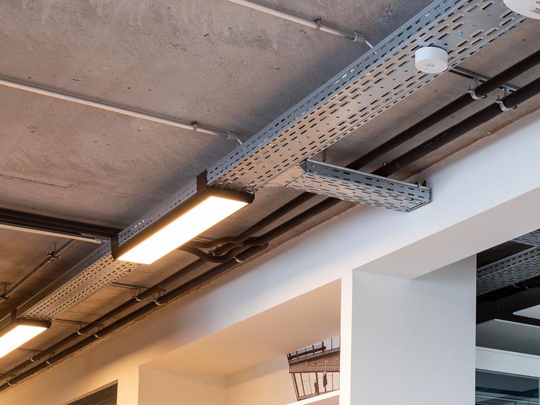 Eine von der Decke hängende, nicht lackierte Kabelrinne für Deckenlampen, die auf diesem Bild warm-golden leuchten.
