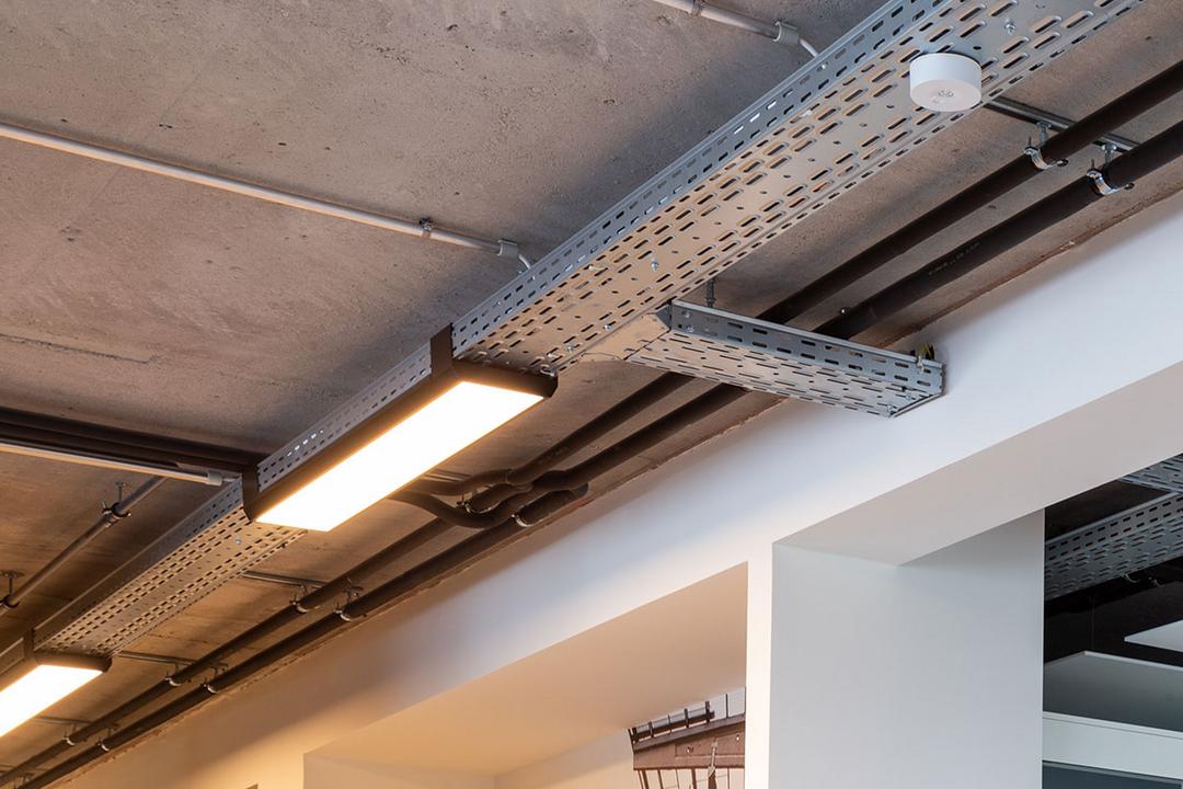 Eine von der Decke hängende, nicht lackierte Kabelrinne für Deckenlampen, die auf diesem Bild warm-golden leuchten.