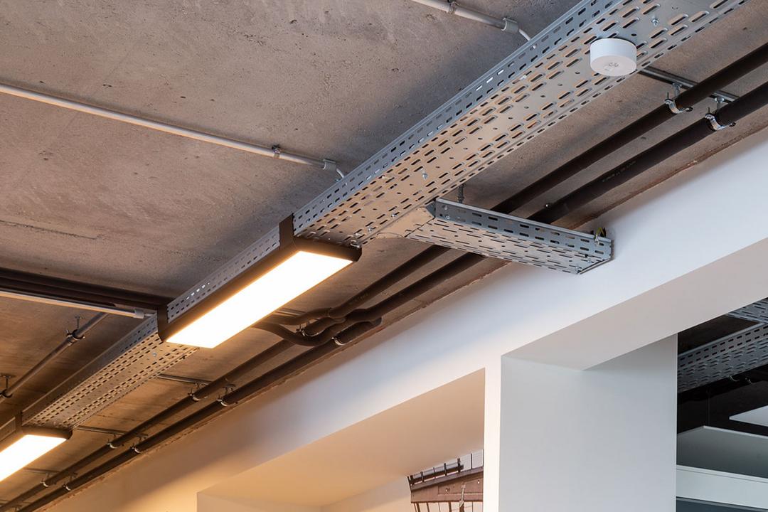 Eine von der Decke hängende, nicht lackierte Kabelrinne für Deckenlampen, die auf diesem Bild warm-golden leuchten.