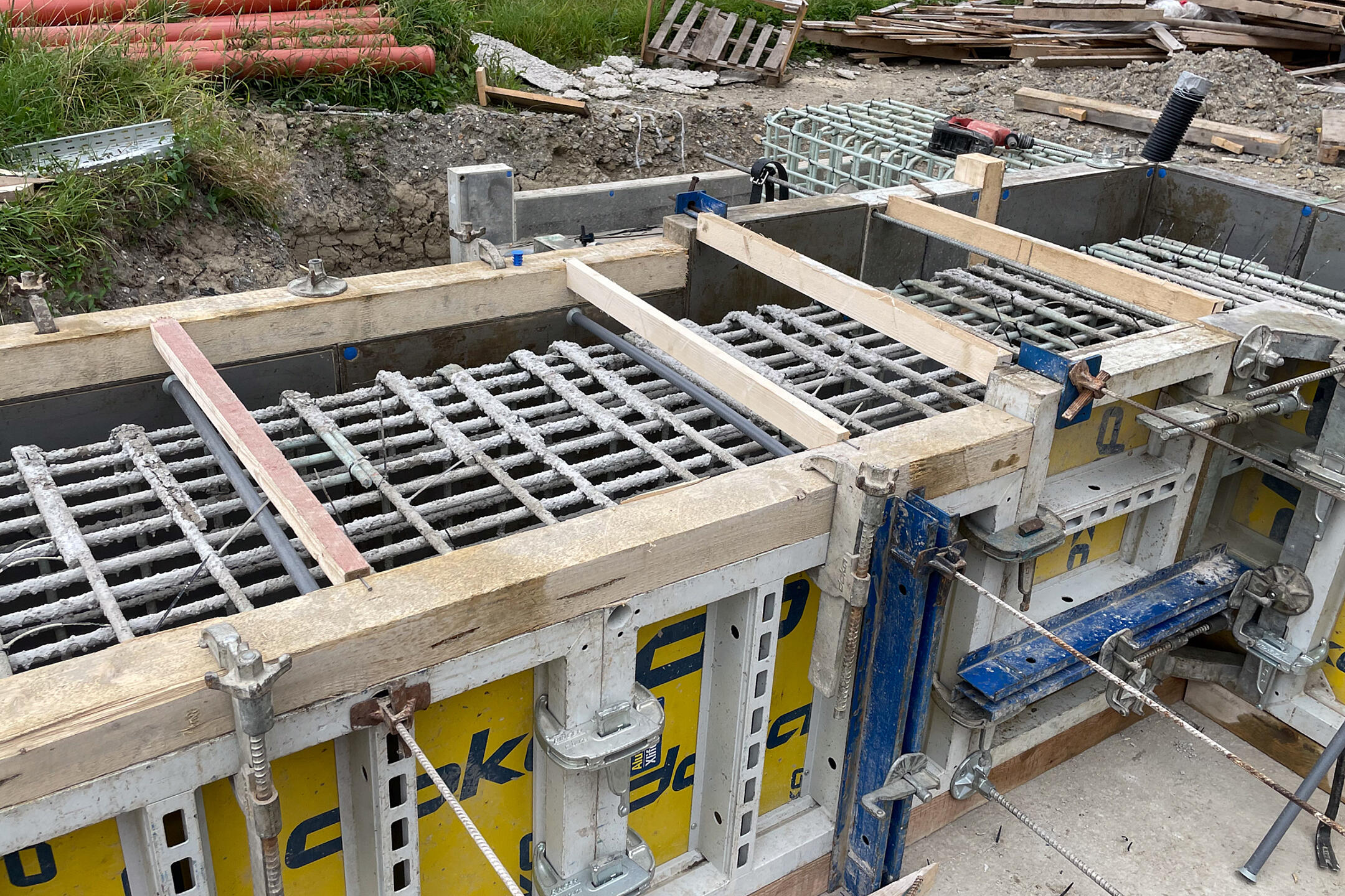 GFK-Bewehrung in Holz-Metall-Verkleidung, im Hintergrund sind Paletten und Rohre zu sehen.