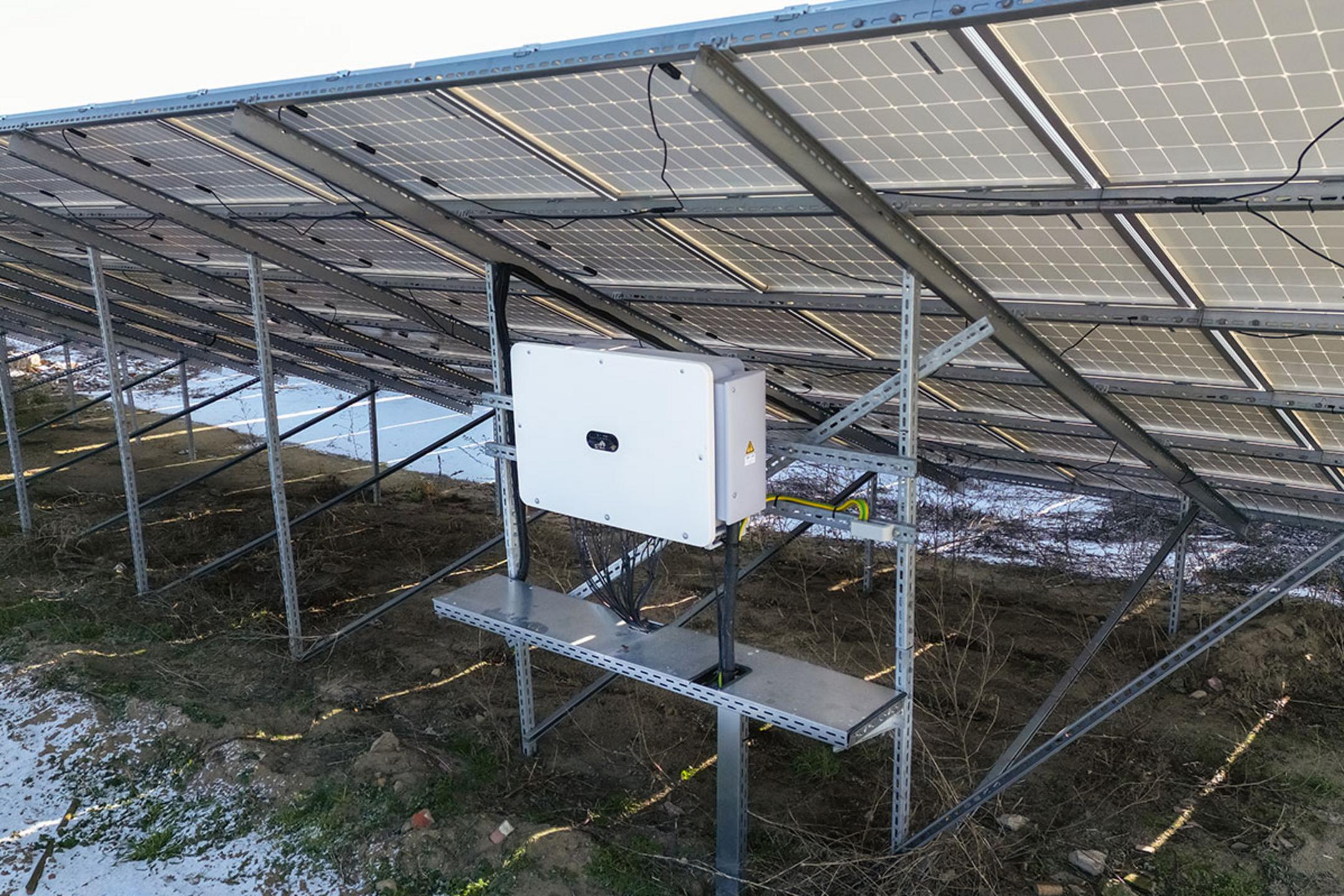 Solarmodule auf Stützen montiert mit angeschlossenem Wechselrichter, darunter Vegetation und Schneereste