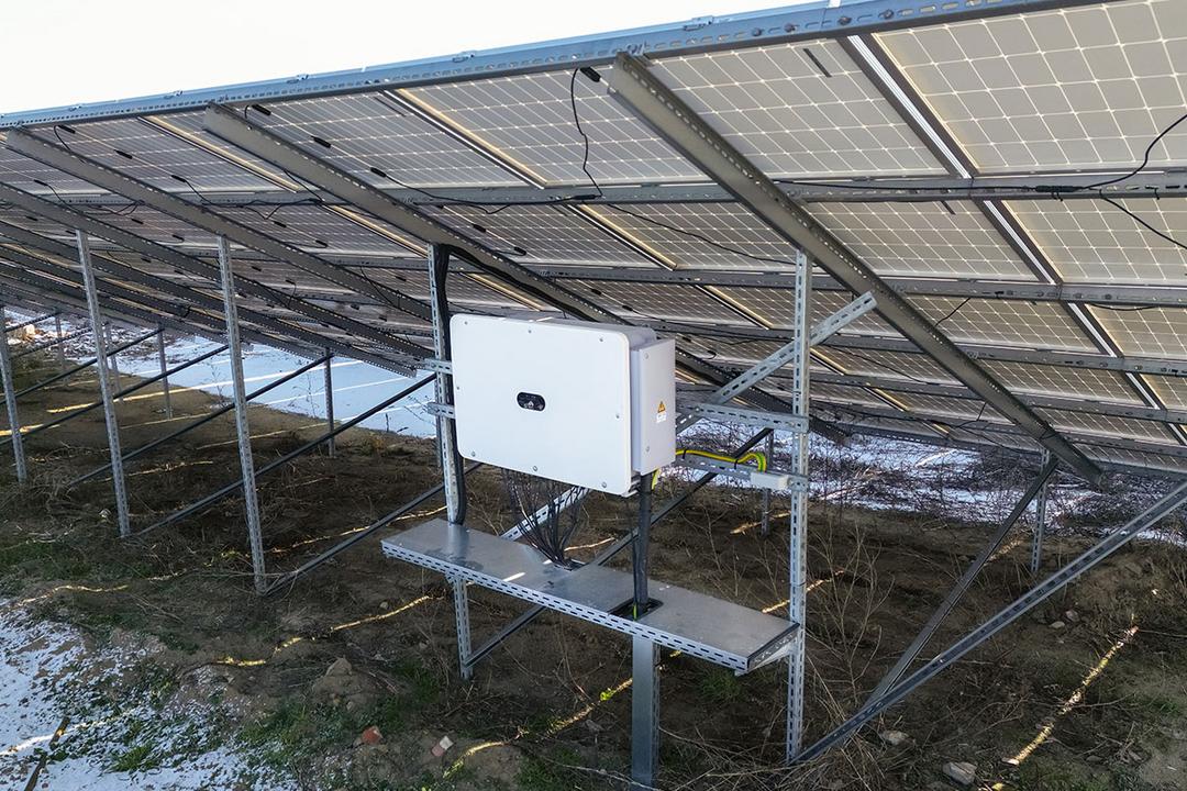 Solarmodule auf Stützen montiert mit angeschlossenem Wechselrichter, darunter Vegetation und Schneereste