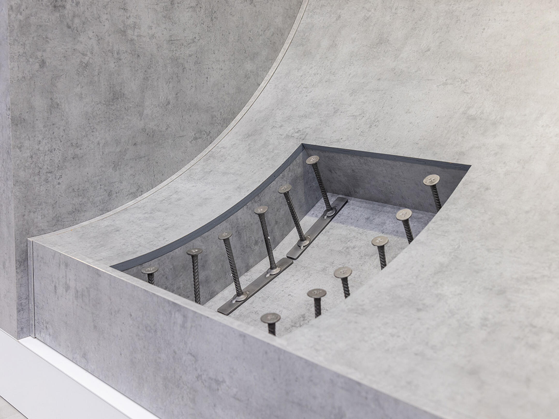 Ausstellungsmodell eines Tunnelbauteils mit eingebauten Ankern und Verbindungselementen in einer Betonvertiefung.