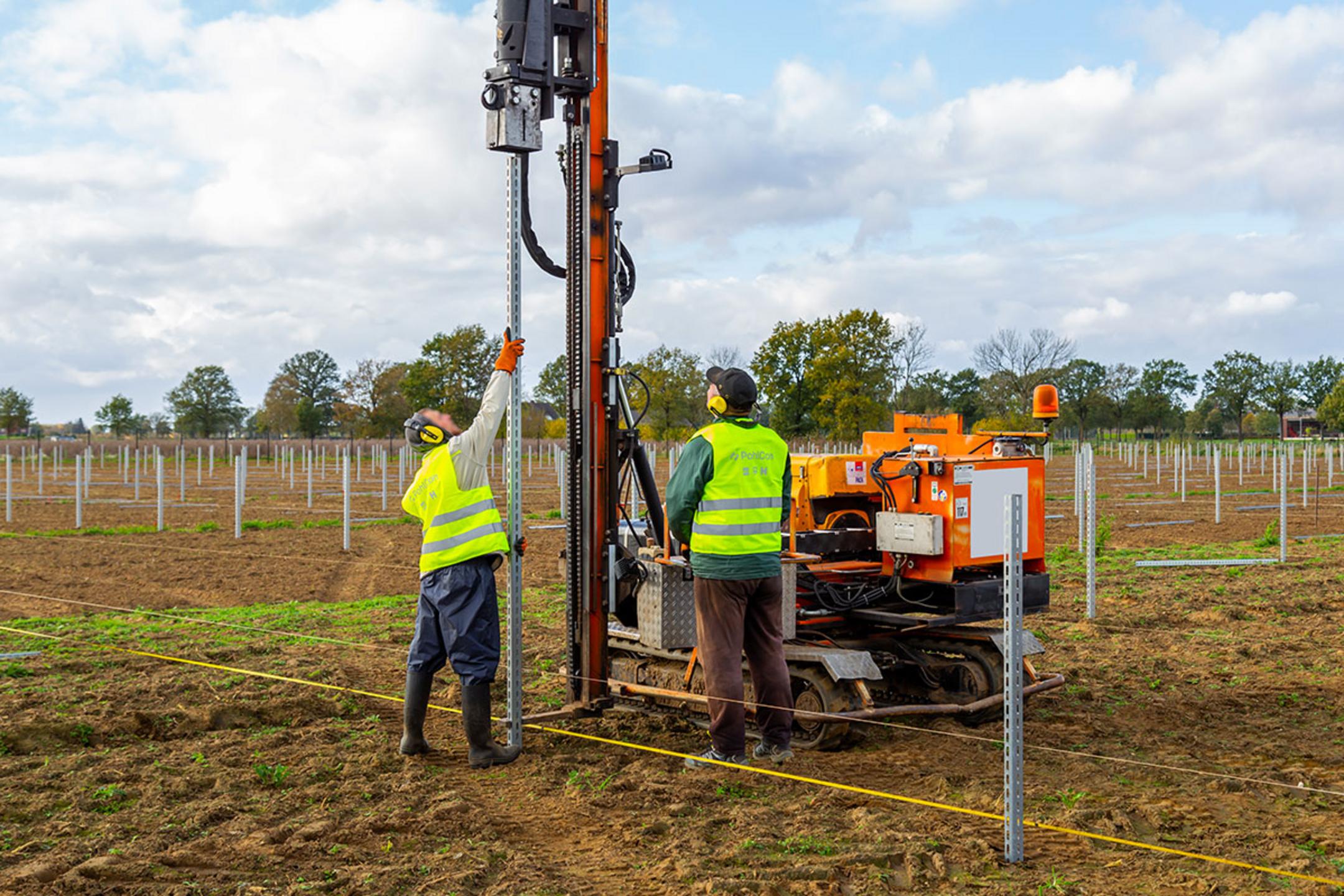 Arbeiter bei der Rammung von Stützprofilen in einem Solarpark, unterstützt durch eine Maschine
