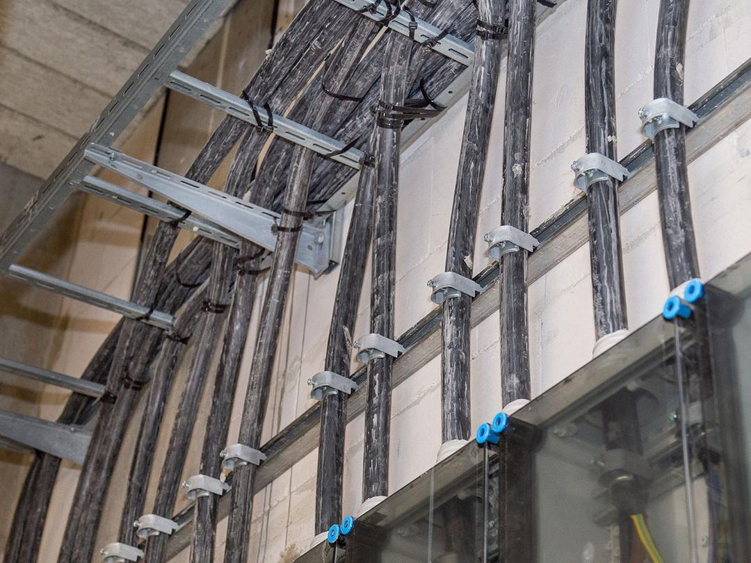 Viele Kabel verlaufen durch transparente Führungsrohre an einer Wand herunter.