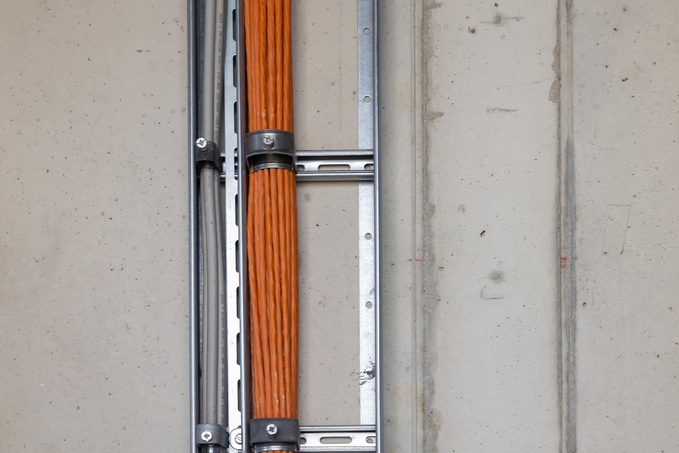 Betonwand mit Steigetrasse, in der Bündel von Kabeln verlaufen, die mit Kabelschellen befestigt sind.