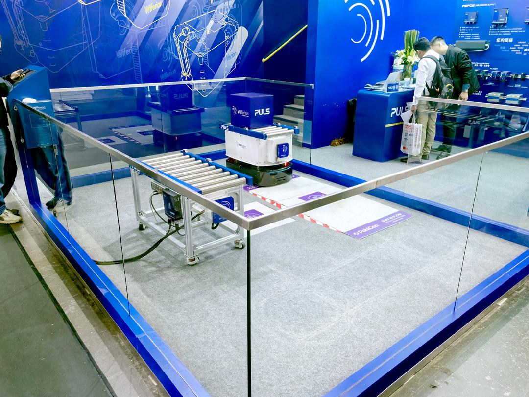 Ein Roboter vor einer Ladestation im Boden in einer Glasshowcase auf einer Messe.