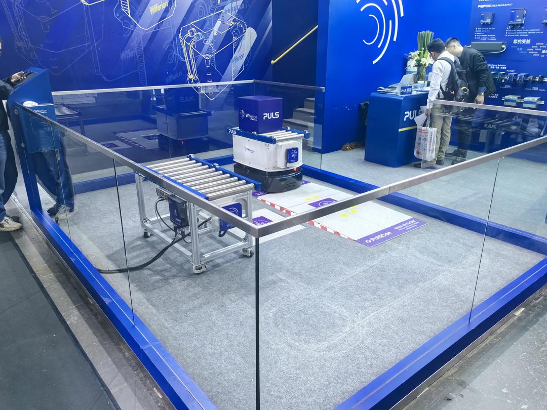 Ein Roboter vor einer Ladestation im Boden in einer Glasshowcase auf einer Messe.