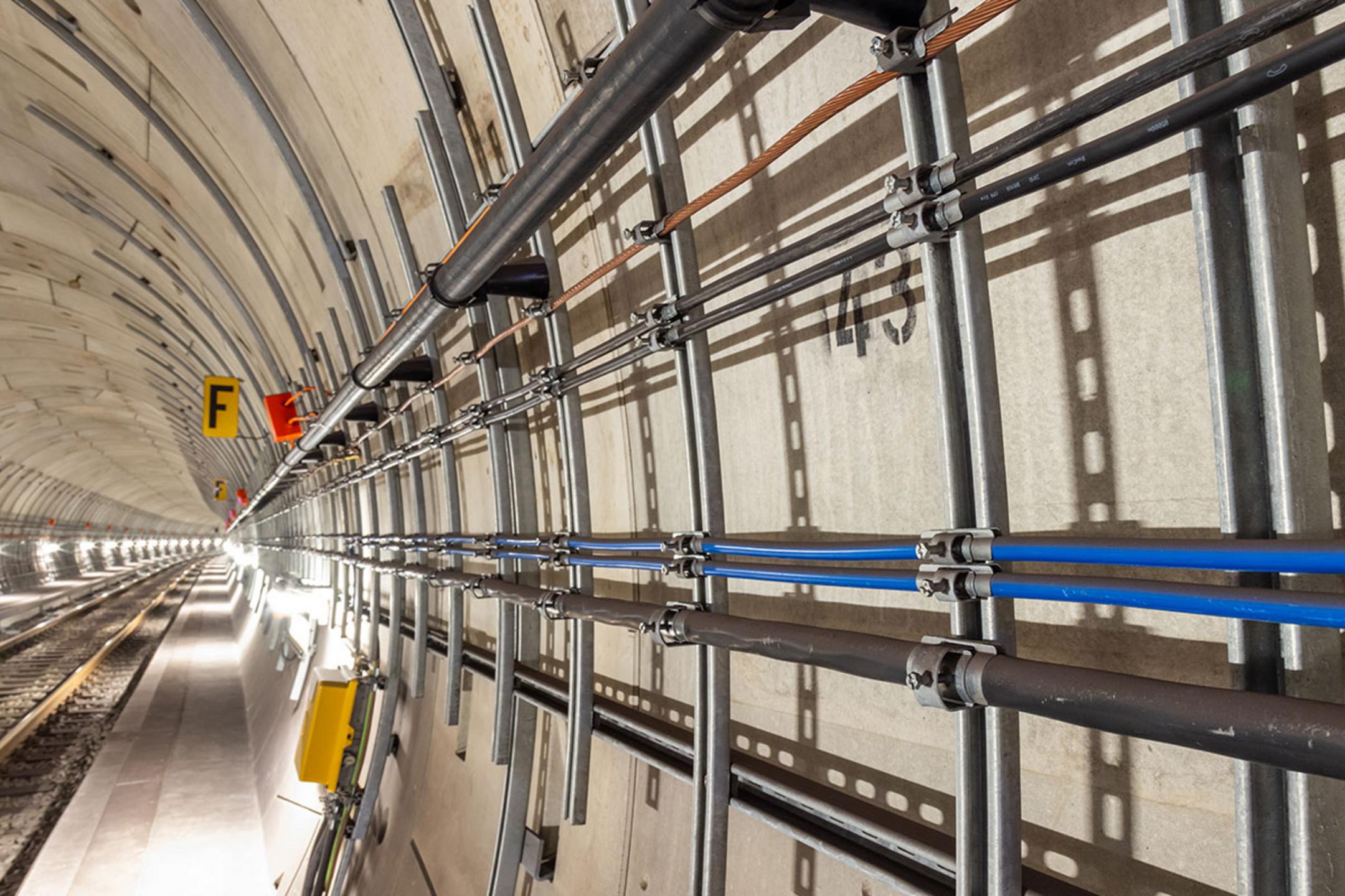 Nahaufnahme von Profilschienen mit schwarzen und blauen Kabeln an der Tunnelwand neben Schienen