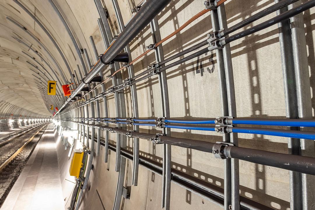 Nahaufnahme von Profilschienen mit schwarzen und blauen Kabeln an der Tunnelwand neben Schienen