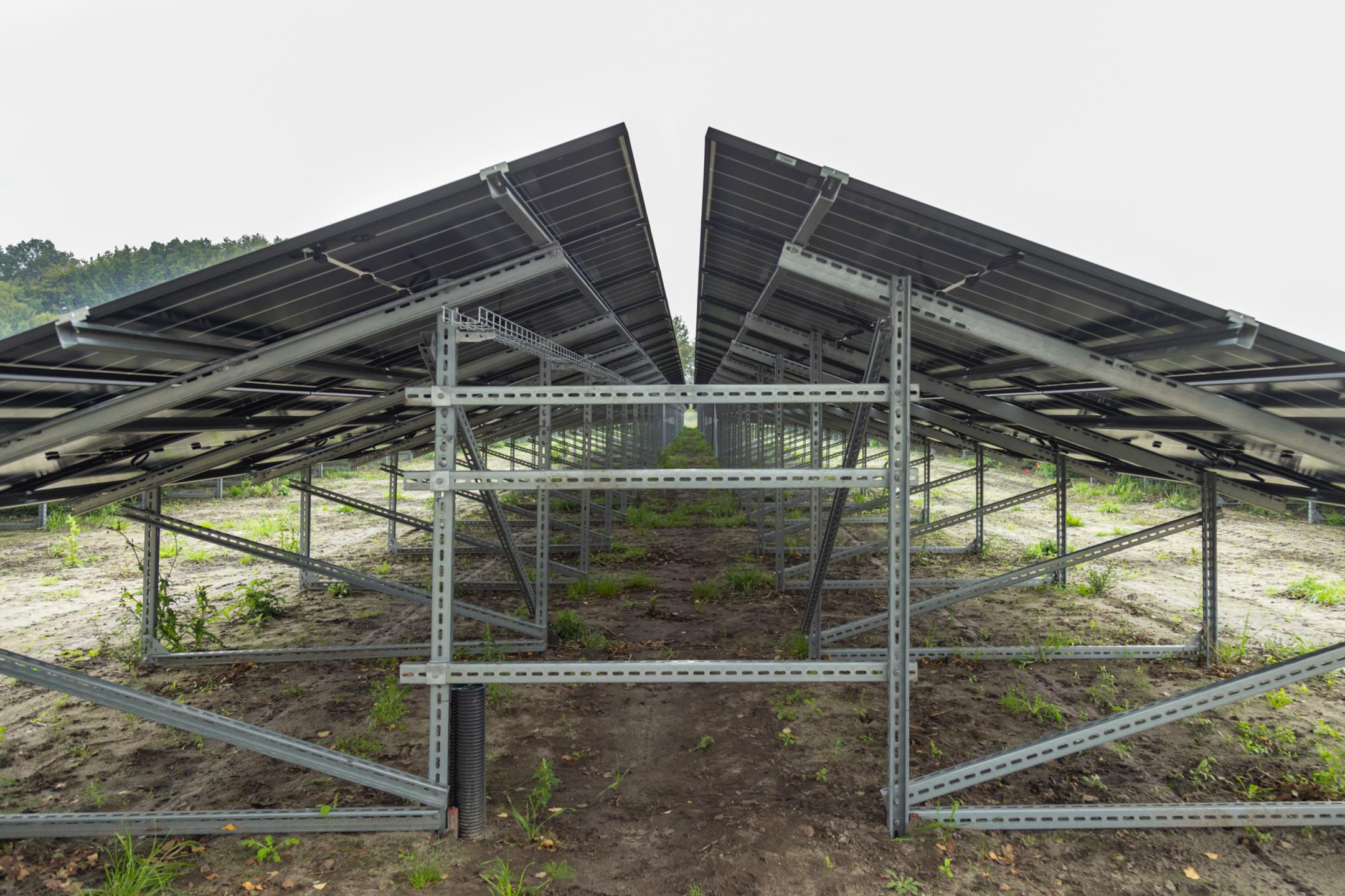 Nahaufnahme einer Unterkonstruktion für Solarmodule auf erdigem Boden, im Hintergrund ein bewölkter Himmel.