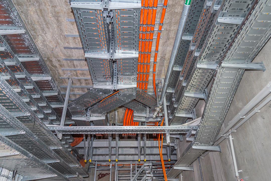 Blick in einen Versorgungsschacht mit vielen Kabelrinnen und orangen Kabeln an Betonwänden und -decke