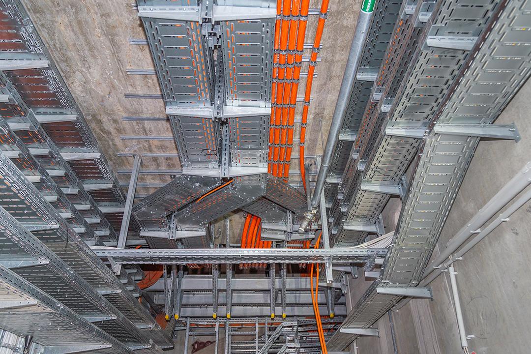 Blick in einen Versorgungsschacht mit vielen Kabelrinnen und orangen Kabeln an Betonwänden und -decke