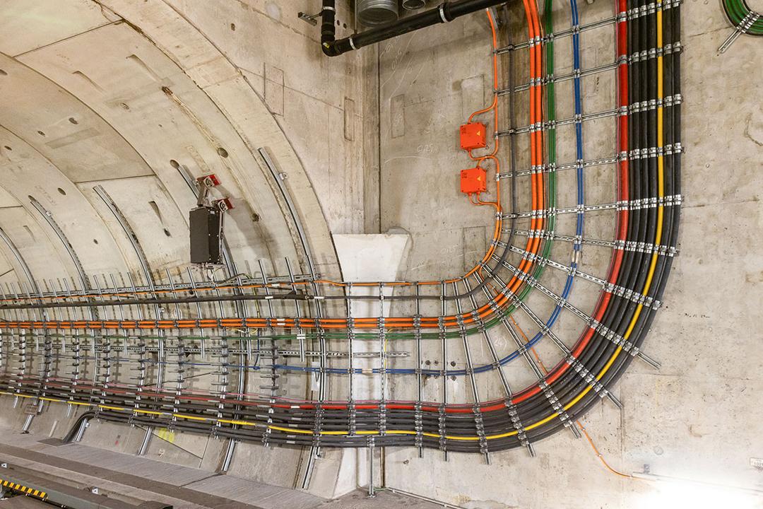 Präzise verlegte farbcodierte Kabel in einem Tunnel, geführt in Halterungen entlang der Wand