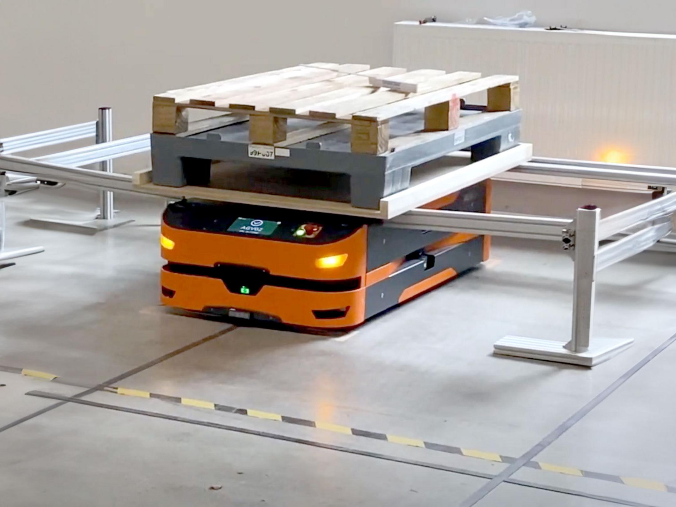 Oranger fahrerloser Transportroboter mit zwei Paletten in einem Lager, umgeben von Absperrungen