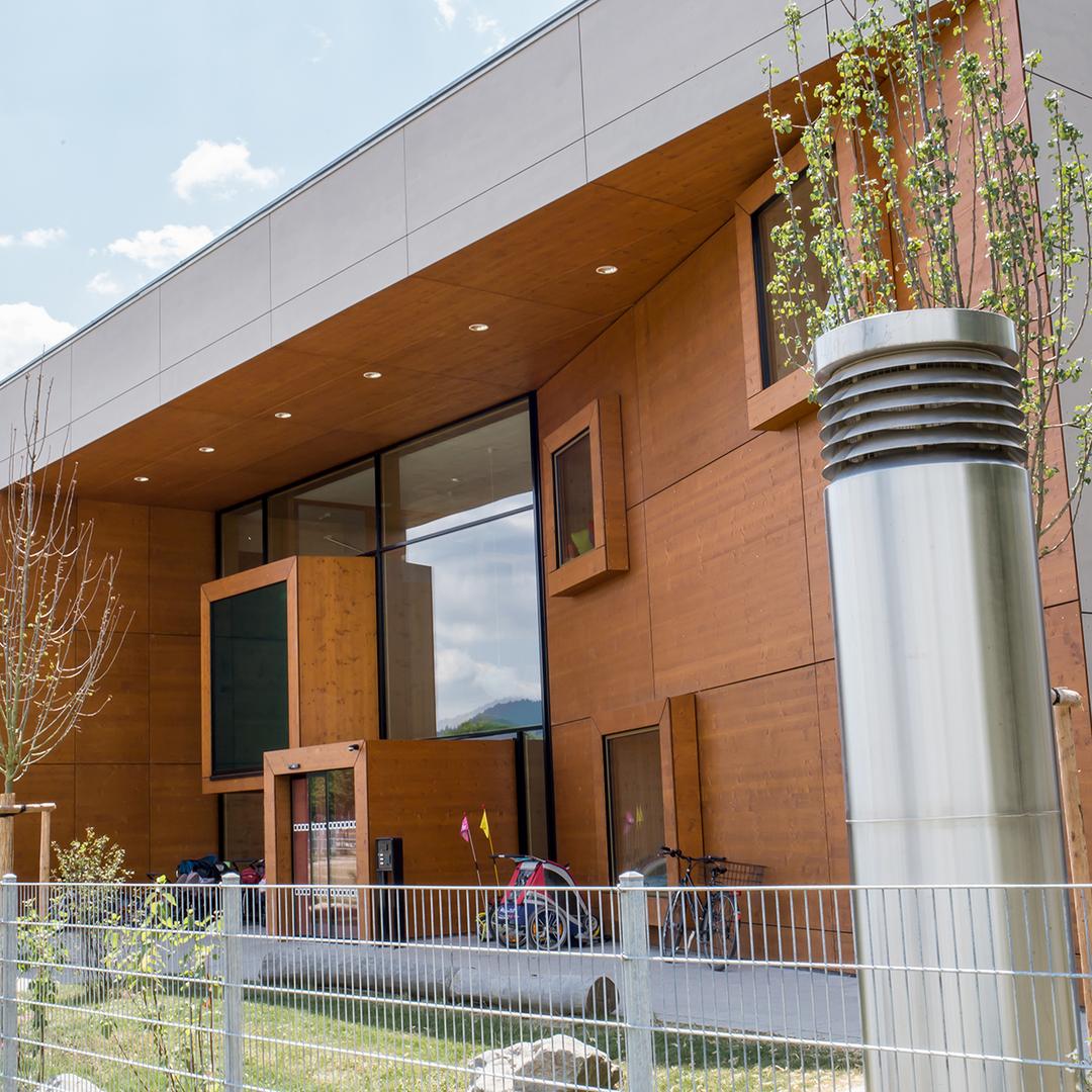 Modernes Gebäude mit Holzfassade, Glasfront, Metallstruktur, Fahrrädern und jungen Bäumen bei klarem Himmel