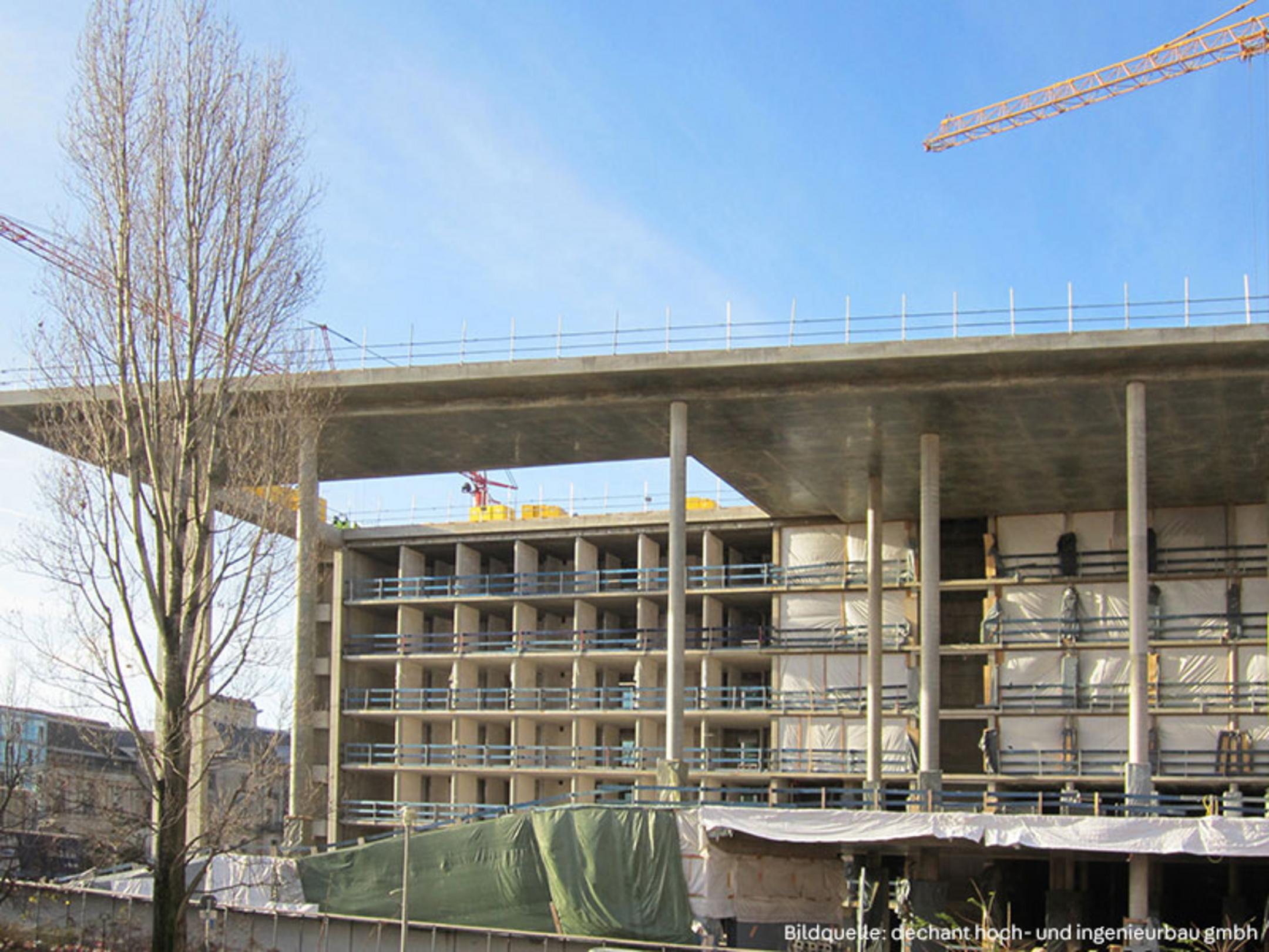 Baustelle mit mehrstöckigem Rohbau, Betonstützen, Kränen im Hintergrund und grünen und weißen Planen am Gebäude