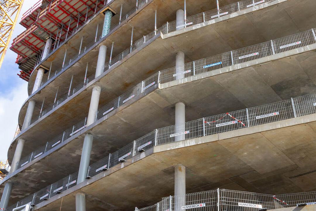 Baugerüst und Schalung auf einer Baustelle, mit sichtbarem Betonpfeiler und Stützen für das nächste Stockwerk