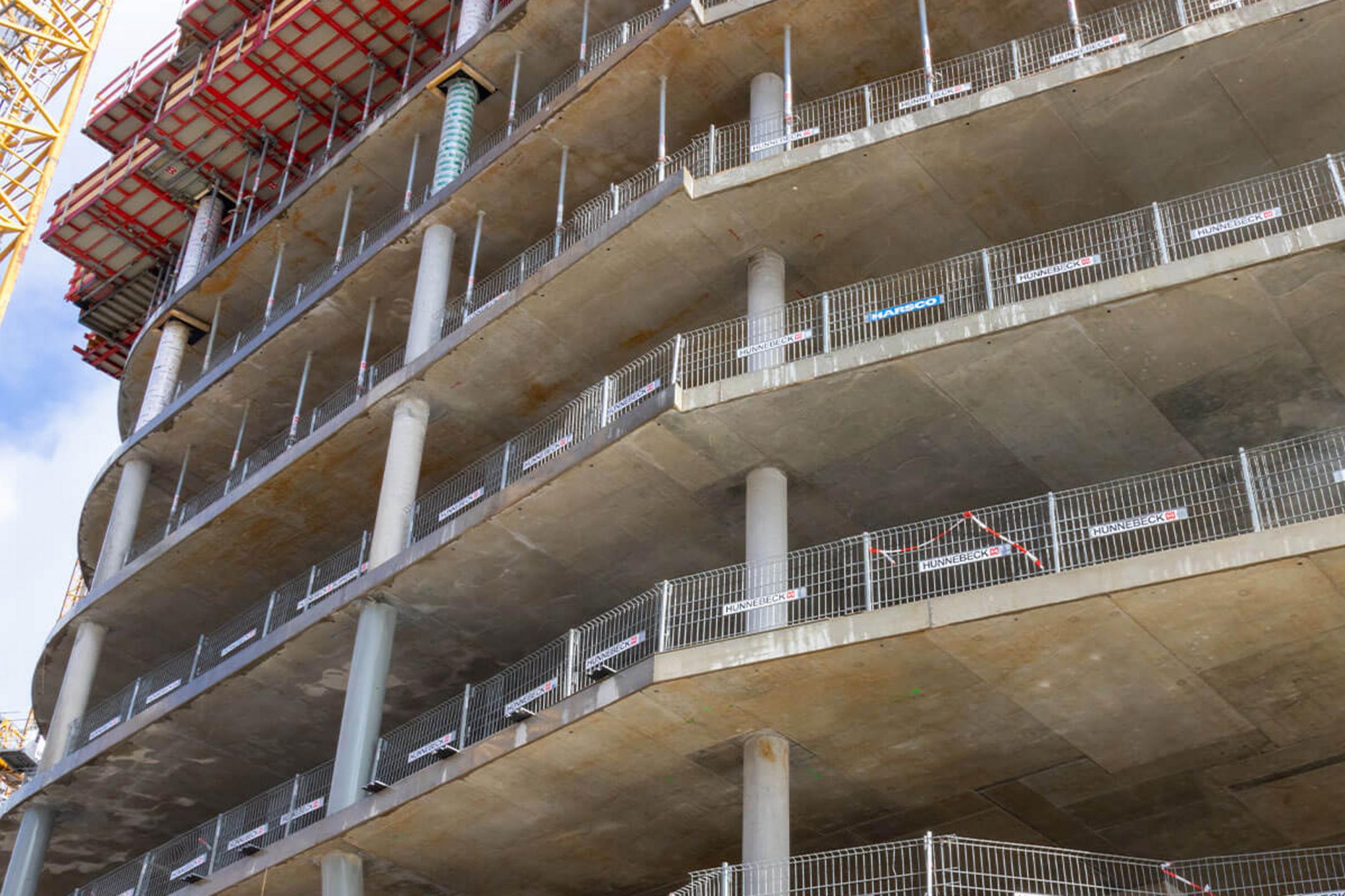 Baugerüst und Schalung auf einer Baustelle, mit sichtbarem Betonpfeiler und Stützen für das nächste Stockwerk