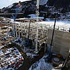 Große Baustelle im Gebirge mit Schnee, Kränen, Stahlgerüst, Betonwänden und Baumaschinen