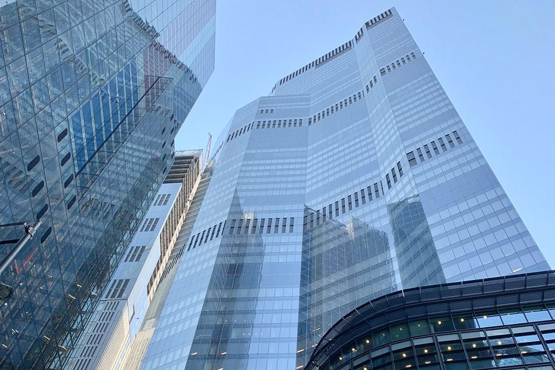 Blick von unten auf das Hochhaus in der 8 Bishopsgate. In der großzügigen Glasfassade spiegelt sich der blaue Himmel.