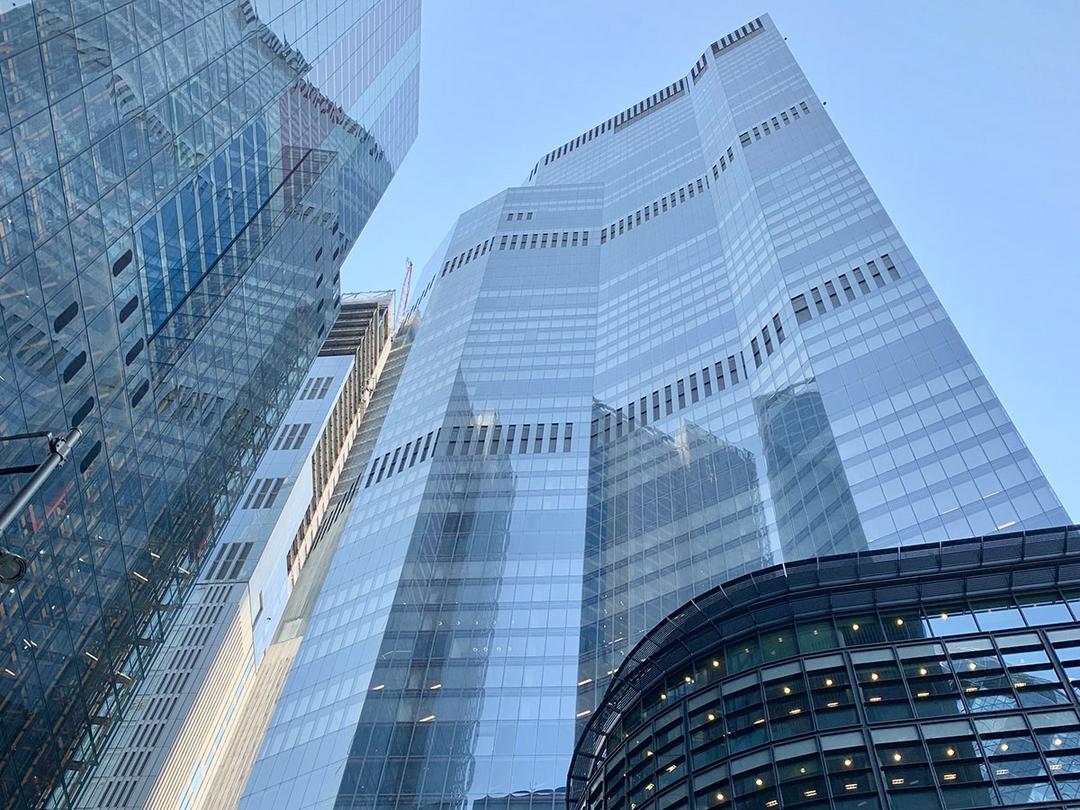 Blick von unten auf das Hochhaus in der 8 Bishopsgate. In der großzügigen Glasfassade spiegelt sich der blaue Himmel.