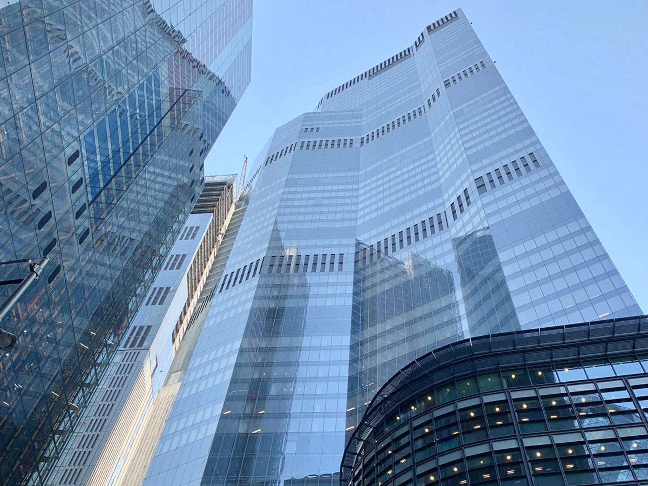 Blick von unten auf das Hochhaus in der 8 Bishopsgate. In der großzügigen Glasfassade spiegelt sich der blaue Himmel.