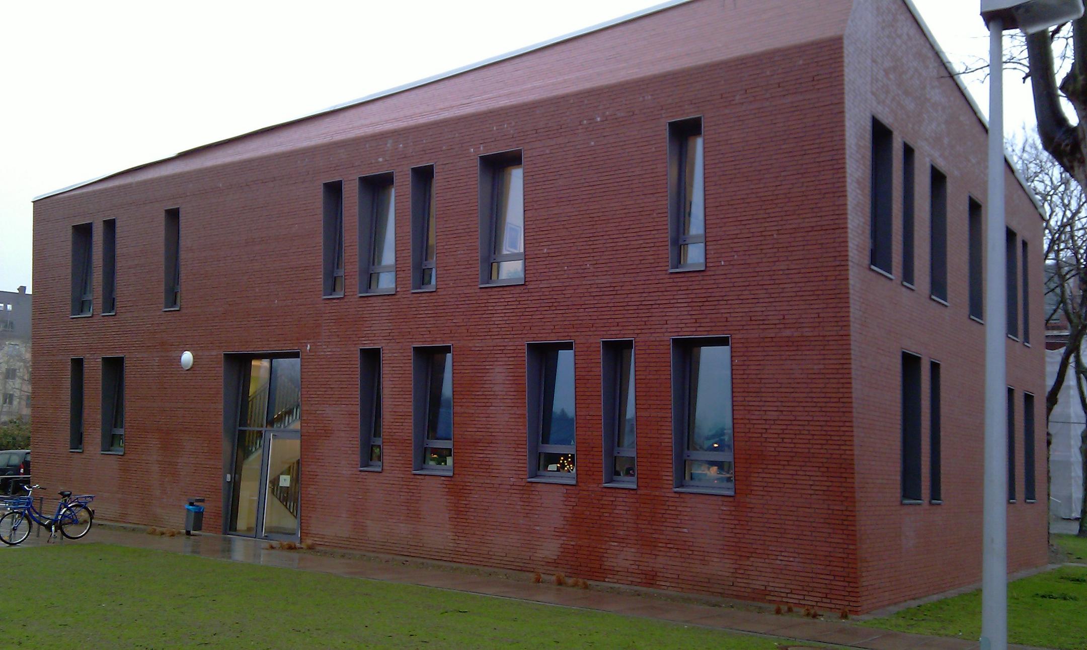 Modernes Backsteingebäude mit schmalen Fenstern, flachem Dach und Eingang an der Seite.