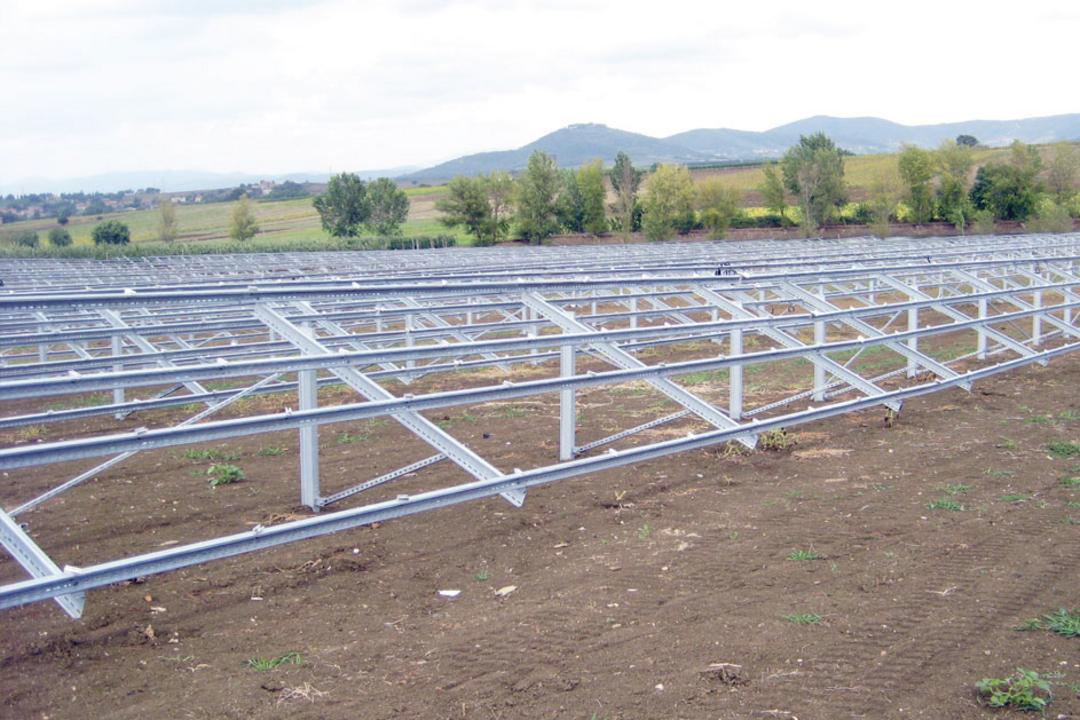 Montierte Stahlunterkonstruktion für eine PV-Anlage auf freiem, ebenem Ackerboden mit Blick auf eine hügelige Landschaft im Hintergrund.