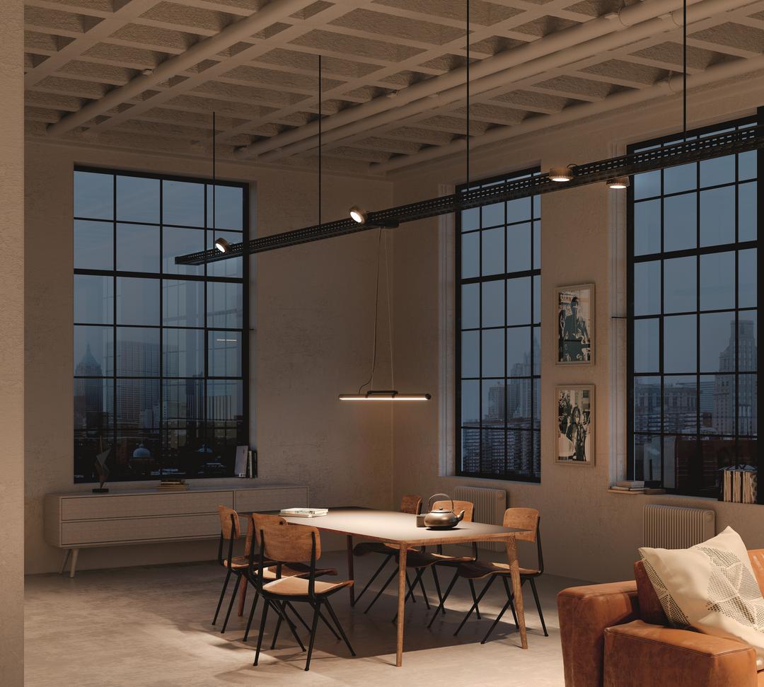 Blick in einen weiteren Raum, der im Industrial Chic eingerichtet ist. Hier handelt es sich um einen modernen Wohnraum mit großen Fensterfronten, der in ein gemütliches Licht getaucht ist.