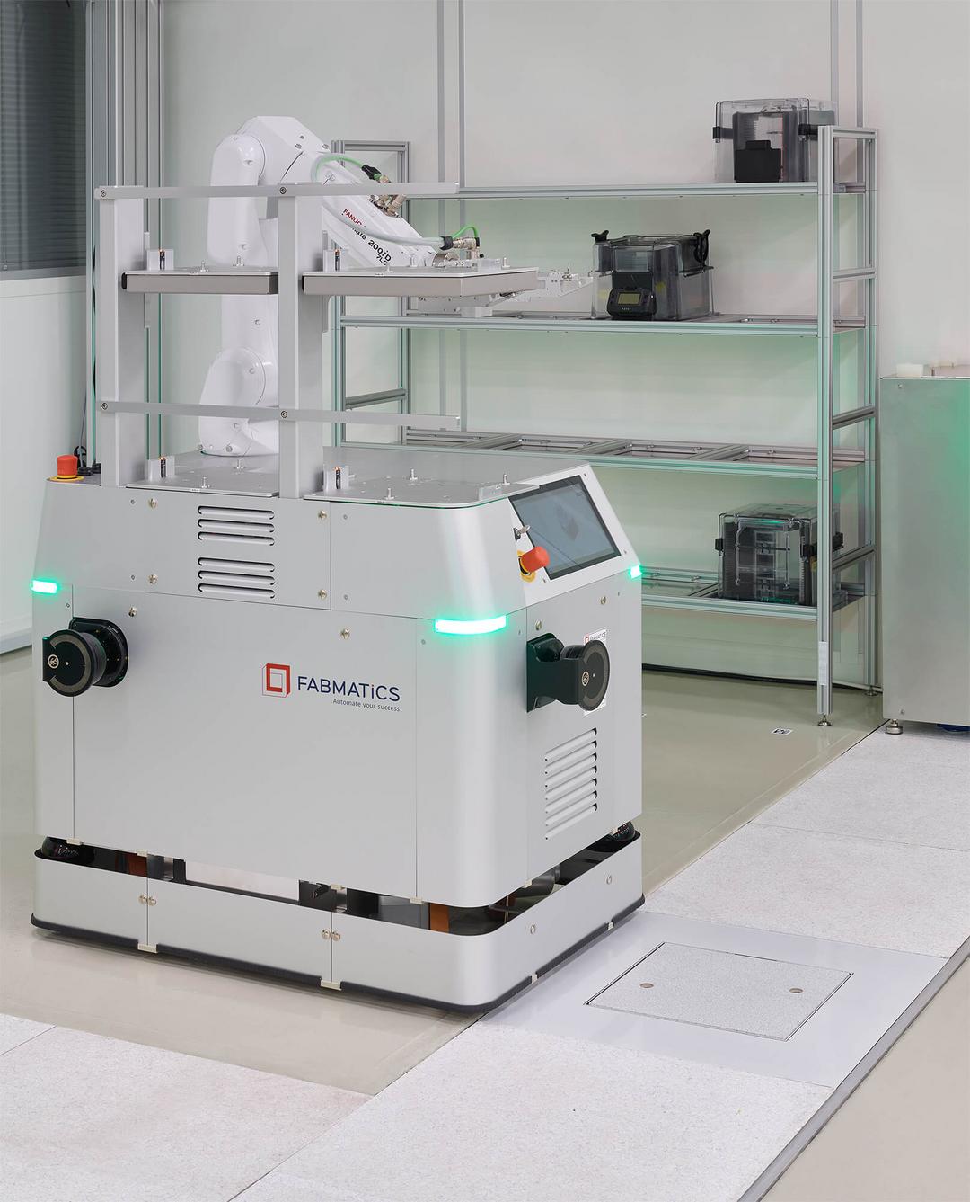 Ein Fabmatics-Roboter, der über eine Wireless Charging Protection System (WCPS)-Ladestruktur fährt, aus einer anderen Perspektive, im Hintergrund ein Regal.